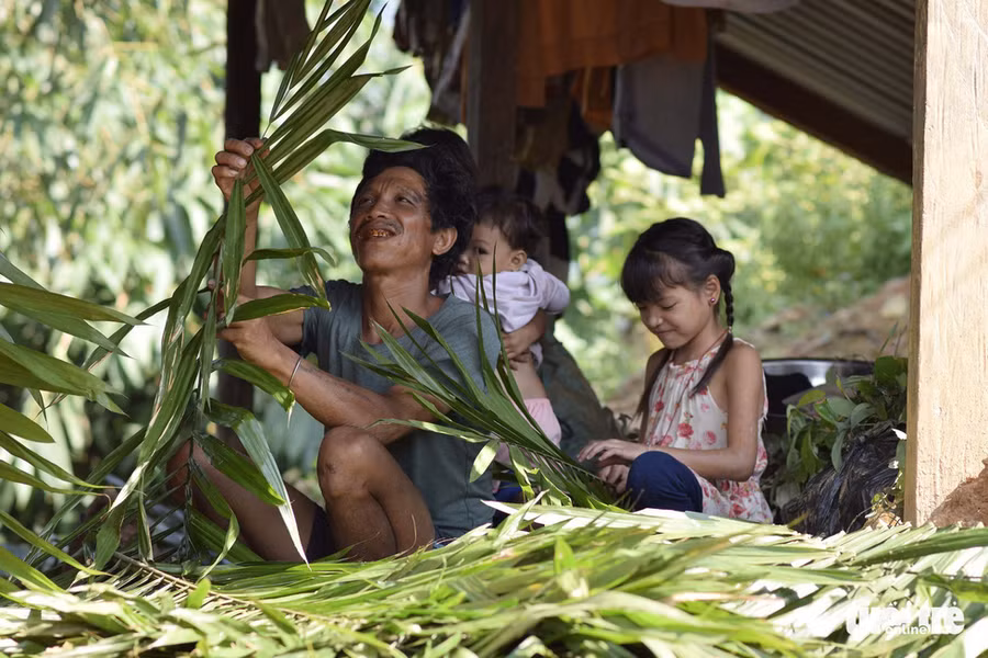 Người đàn ông chuẩn bị lá để thay mái cũ, có cô bé phụ giúp - Ảnh: LÊ VĂN ÁNH