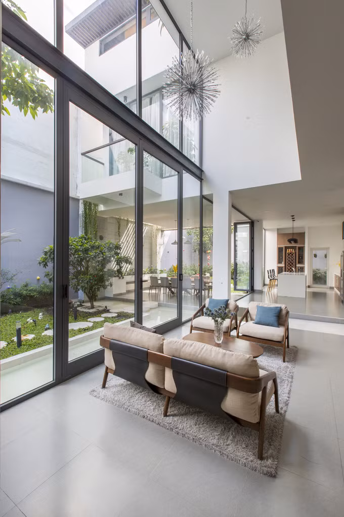 Phòng khách nối liền với khu vực phòng ăn, nhà bếp theo hình chữ L. Nếu tường kính xóa đi ranh giới trong - ngoài thì thông tầng đã xóa nhòa ranh giới giữa bên trên và dưới, giúp phòng khách thông thoáng với không gian mở rộng cả ba chiều.