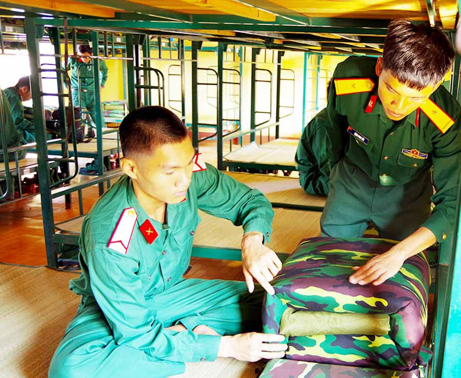 Chiến sĩ mới Lương Sơn Tới đang được cán bộ hướng dẫn gấp chăn. Ảnh: S.T  Chiến sĩ mới Lương Sơn Tới đang được cán bộ hướng dẫn gấp chăn. Ảnh: S.T