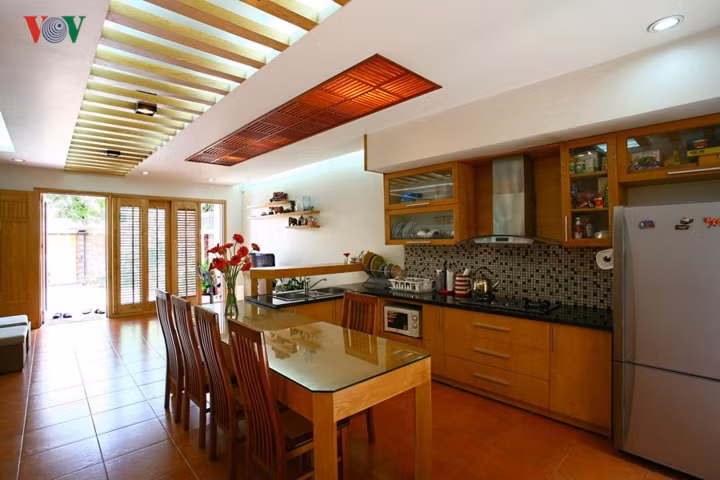  Phòng bếp với không gian mở. Cách tổ hợp bàn ăn liền với hệ thống tủ bếp, quầy bar tạo nên một không gian cô đọng, kín đáo hơn cho khu bếp và thuận tiện cho sinh hoạt. Chất liệu gỗ của cửa và đồ nội thất gợi cảm giác gần gũi nhưng vẫn hiện đại và mang phảng phất nét Á Đông