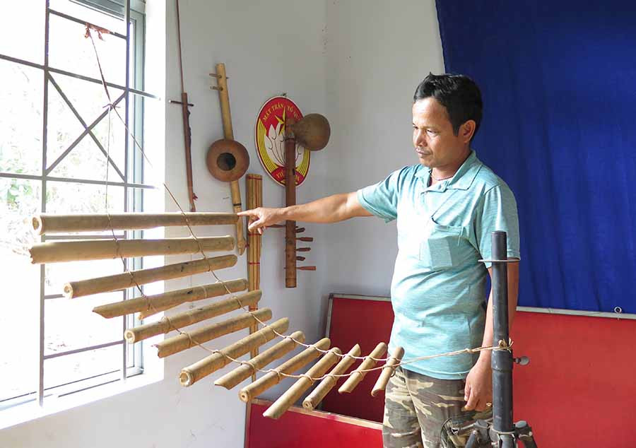 Anh Huân bên góc trưng bày nhạc cụ trong nhà sinh hoạt cộng đồng của làng. Ảnh: P.L  Anh Huân bên góc trưng bày nhạc cụ trong nhà sinh hoạt cộng đồng của làng. Ảnh: P.L