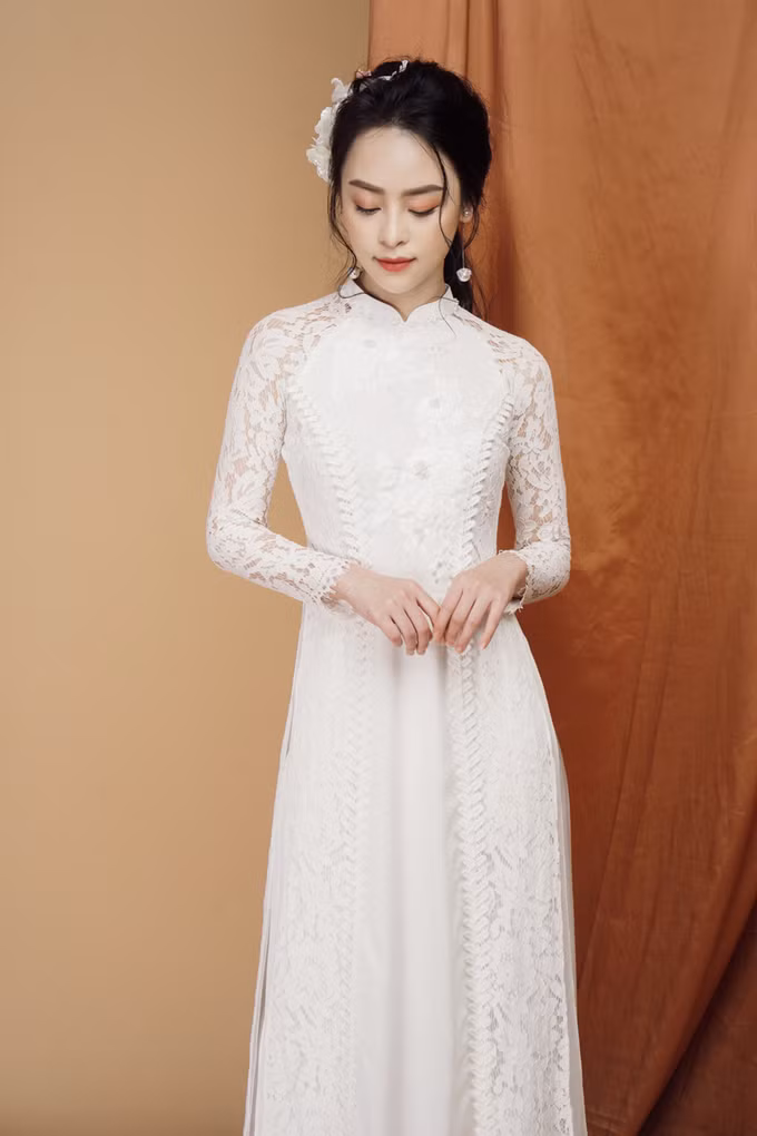 Mẫu áo dài ren được thêu hoa trắng trên ngực tô thêm nét đẹp tinh khôi, e ấp của nàng dâu mới. Dải dây leo chạy dọc thân giúp kéo dài chiều cao cơ thể của người mặc.