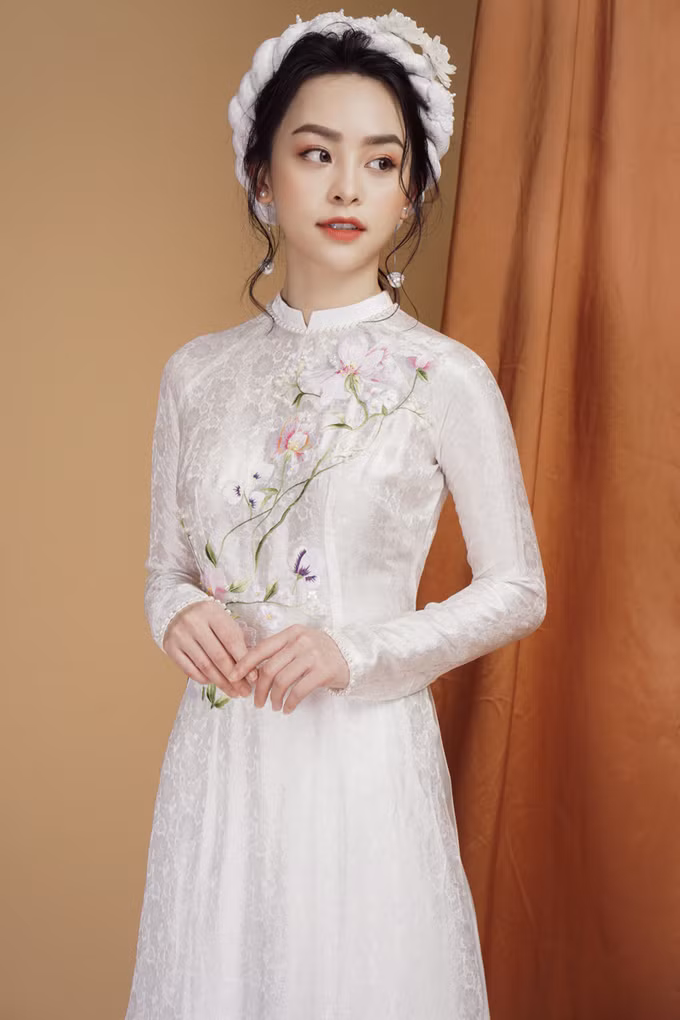  Áo dài trắng tinh khôi là lựa chọn tiếp theo dành cho bạn gái trong dịp hỷ sự. Họa tiết thêu được chạy chéo từ cầu vai đến eo tạo nét duyên dáng cho cô dâu mới.