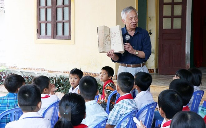 Giáo sư Nguyễn Huy Mỹ - người con của dòng họ Nguyễn Huy trò chuyện với học sinh trường Tiểu học Trường Lộc (Hà Tĩnh) về cuốn sách “Hoàng hoa sứ trình đồ.” (Ảnh: TTXVN)