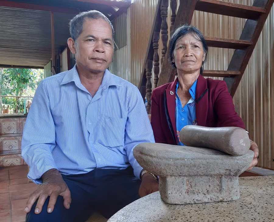 Vợ chồng ông Rơ Châm Phih bên bộ bàn nghiền của người Chăm ngày xưa. Ảnh: Nguyễn Quang Tuệ