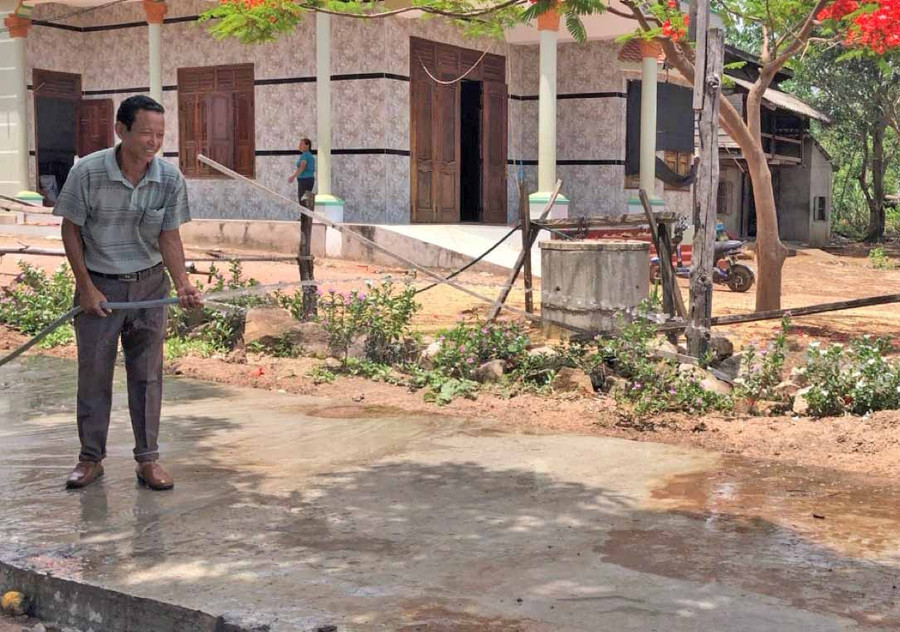 ông Thủy đang tưới nước đoạn đường bê tông vừa mới hoàn thiện