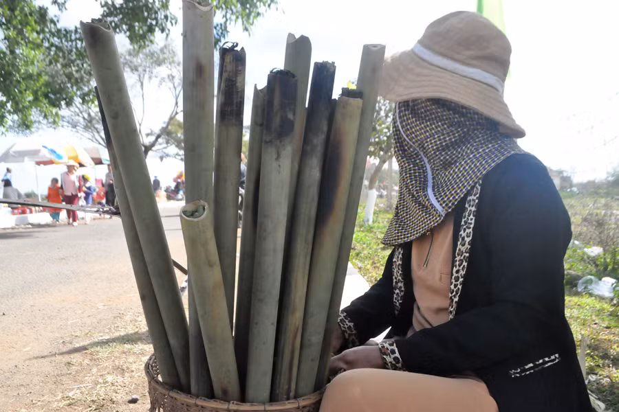 Những người phụ nữ bán cơm lam ngồi nép mình bên chiếc gùi, bẽn lẽn nhìn dòng người vui xuân. Ảnh: Trần Dung