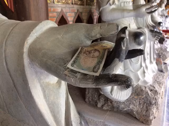Người đi lễ chùa vô tư đặt tiền lên tay phật ở chùa Bái Đính.
