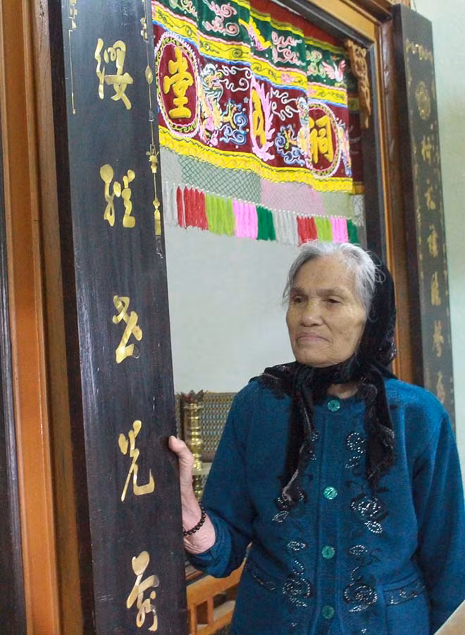 Cụ Diệp Thị Hà bên câu đối bằng gỗ vẫn còn lưu giữ của dòng họ Nguyễn. Ảnh: H.T