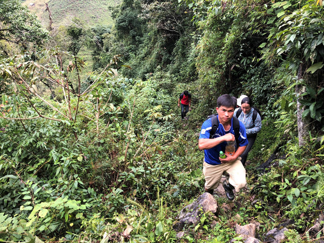Thầy giáo Hò Văn Lợi đi vận động HS đến trường, trên tay là chai nước lá rừng