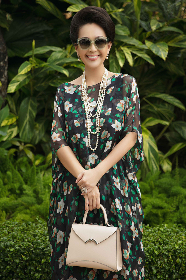 "Nữ hoàng ảnh lịch" Diễm My chọn thiết kế phom rộng, nhiều lớp với chất liệu chiffon mỏng tang. Trên nền đen, họa tiết hoa lá màu trắng, cam, xanh hòa quyện thành điểm nhấn. Nữ diễn viên phối bộ cánh cùng vòng cổ ngọc trai Chanel và giày, túi xách màu nude thanh lịch.