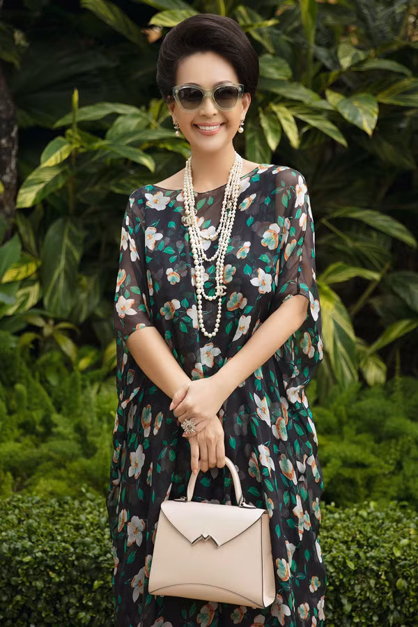 "Nữ hoàng ảnh lịch" Diễm My chọn thiết kế phom rộng, nhiều lớp với chất liệu chiffon mỏng tang. Trên nền đen, họa tiết hoa lá màu trắng, cam, xanh hòa quyện thành điểm nhấn. Nữ diễn viên phối bộ cánh cùng vòng cổ ngọc trai Chanel và giày, túi xách màu nude thanh lịch.
