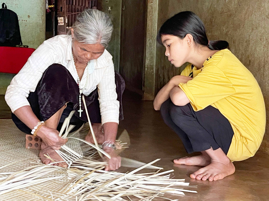 Bà Rơ Mah Suét hướng dẫn kỹ thuật đan chiếu pran cho cháu ngoại Rơ Mah San. Ảnh: Hồng Ngọc