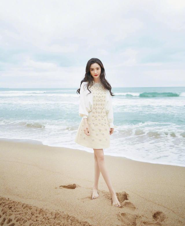 Người đẹp diện váy ngắn màu kem đính ngọc trai để chân trần trên cát, trang điểm tự nhiên với mái tóc xoăn nhẹ bồng bềnh rất nữ tính và ngọt ngào.