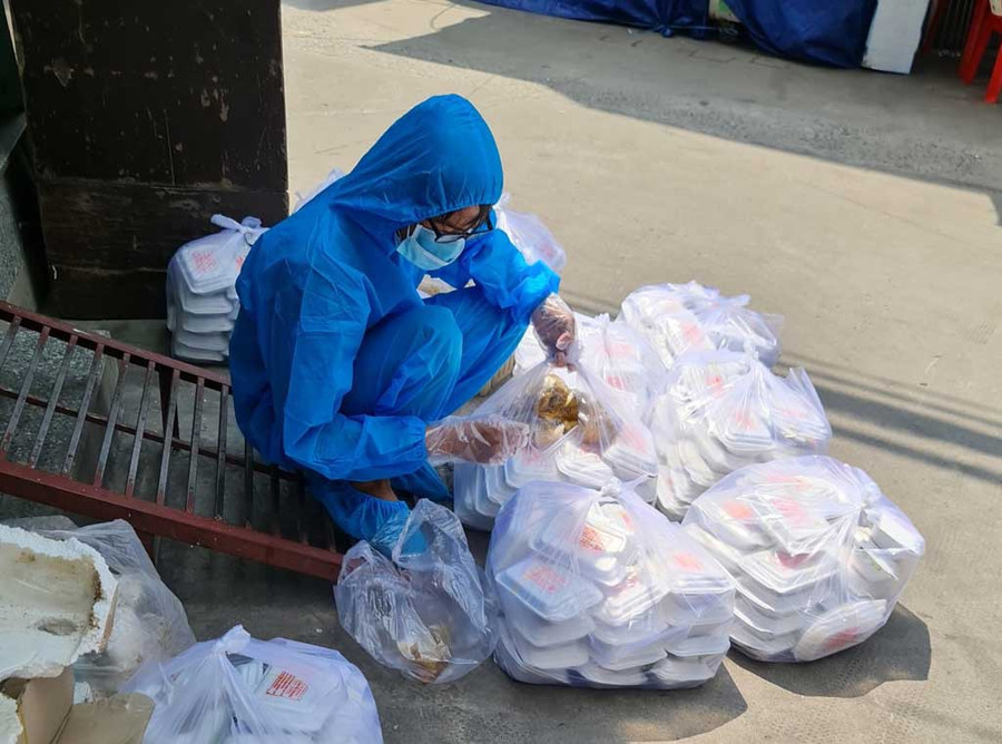 Tình nguyện viên soạn cơm xách vào bên trong các hẻm nhỏ để phát. ẢNH: NAM NGUYỄN