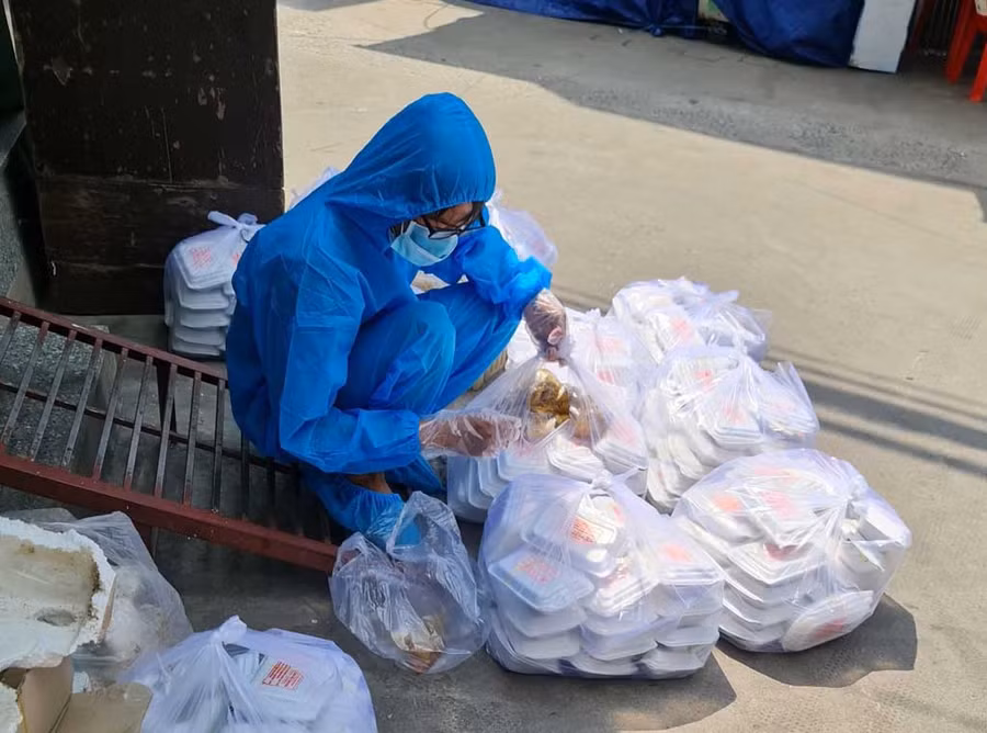 Tình nguyện viên soạn cơm xách vào bên trong các hẻm nhỏ để phát. ẢNH: NAM NGUYỄN