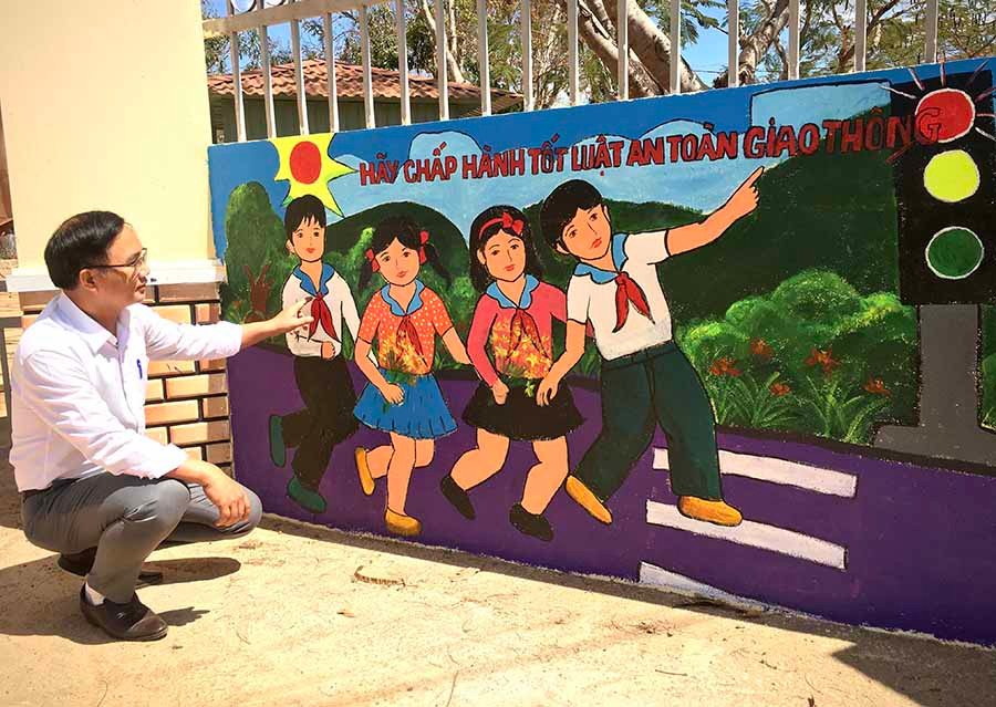  Thầy Võ Văn Thiết bên bức tranh tuyên truyền hành vi giao thông an toàn phía trước cổng trường. Ảnh: H.L