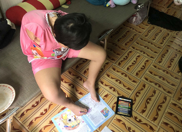 Ân dùng chân tô màu lên cuốn vở vẽ được người ta cho - Ảnh: DIỆU QUÍ