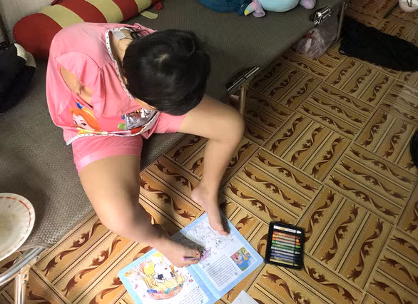 Ân dùng chân tô màu lên cuốn vở vẽ được người ta cho - Ảnh: DIỆU QUÍ
