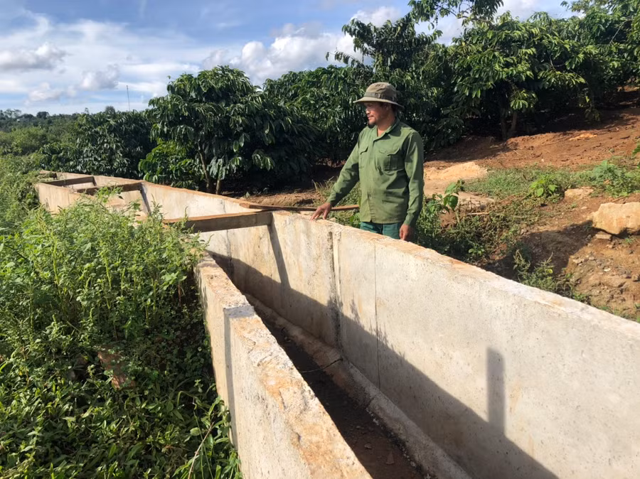 Anh Rơ Châm Hiếu (làng Ó) bên hệ thống kênh thủy lợi đi qua vườn cà phê của gia đình. Ảnh: Phương Dung