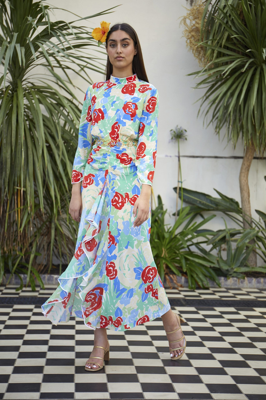  Váy maxi dài quá gối với nhiều bông hoa nhỏ có màu sắc bắt mắt được trang trí xung quanh làm tôn lên vẻ kiều diễm cho các cô nàng, đi kèm là chuỗi dây chuyền thắt eo và sandals cao gót màu vàng ánh kim càng khiến cho set trang phục thêm phần bắt mắt.