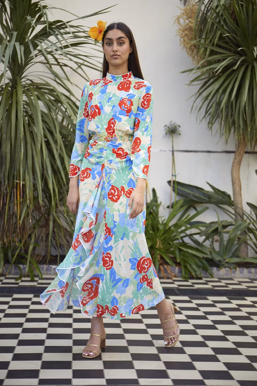  Váy maxi dài quá gối với nhiều bông hoa nhỏ có màu sắc bắt mắt được trang trí xung quanh làm tôn lên vẻ kiều diễm cho các cô nàng, đi kèm là chuỗi dây chuyền thắt eo và sandals cao gót màu vàng ánh kim càng khiến cho set trang phục thêm phần bắt mắt.