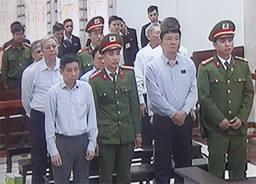 Bảy bị cáo tại phiên tòa, ông Đinh La Thăng đứng ở hàng ghế đầu. Ảnh chụp qua màn hình