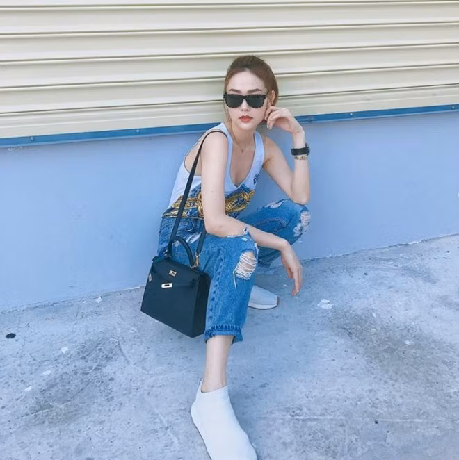  Minh Hằng thả dáng trên phố với áo tank cổ trễ, diện cùng quần jeans rách và giày thể thao bụi phủi. Set đồ có phần nổi loạn của nữ ca sỹ trở nên đắt giá hơn nhờ chiếc túi Kelly của Hermès lên tới hơn 400 triệu đồng.