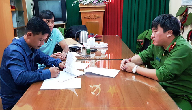 Dân (mặc áo sơ mi dài tay) thực hiện các thủ tục với cơ quan công an trước khi bị bắt tạm giam ẢNH: G.B