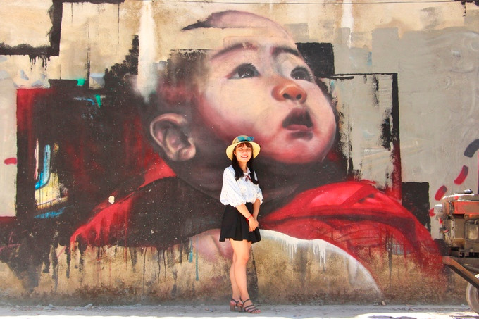  Một bạn trẻ tạo dáng bên bức tranh đứa bé do họa sĩ người Nhật Bản vẽ.