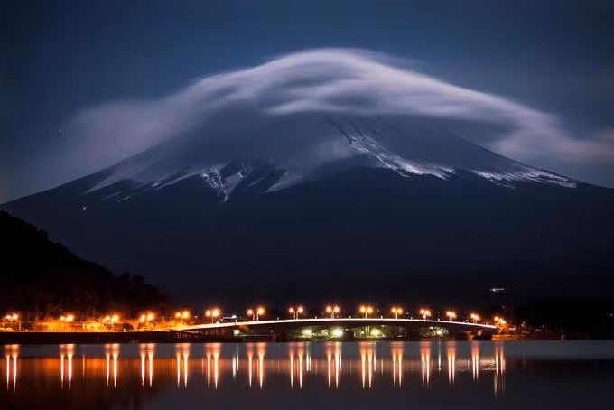 Núi Phú Sĩ phát sáng trong ánh trăng, bên dưới là hồ Kawaguchi được thắp sáng bằng đèn đường cao tốc vào lúc nửa đêm.