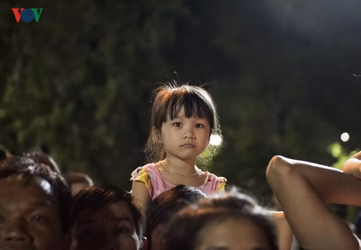 Một em bé chăm chú theo dõi các đội lân thi đấu trên vai của bố.