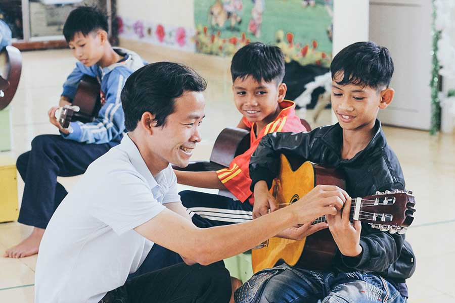 Thầy giáo Lê Văn Nhất trong một buổi dạy đàn cho học sinh Làng trẻ em SOS Pleiku (ảnh do nhóm nhạc họa T&T cung cấp).