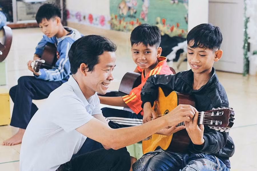 Thầy giáo Lê Văn Nhất trong một buổi dạy đàn cho học sinh Làng trẻ em SOS Pleiku (ảnh do nhóm nhạc họa T&T cung cấp).