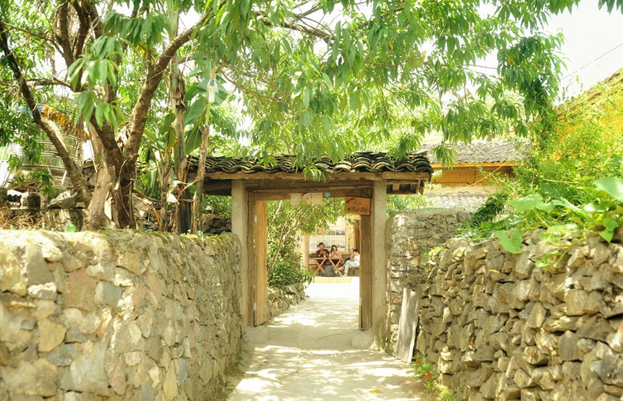 Cổng dẫn vào ngôi nhà, quán cà phê của chị Vấn. Bao quanh bởi tường rào đá, quán mang không gian kiến trúc theo phong cách truyền thống của người Lô Lô, nhà trình tường đắp đất, mái phủ ngói âm dương. Cổng dẫn vào ngôi nhà, quán cà phê của chị Vấn. Bao quanh bởi tường rào đá, quán mang không gian kiến trúc theo phong cách truyền thống của người Lô Lô, nhà trình tường đắp đất, mái phủ ngói âm dương.