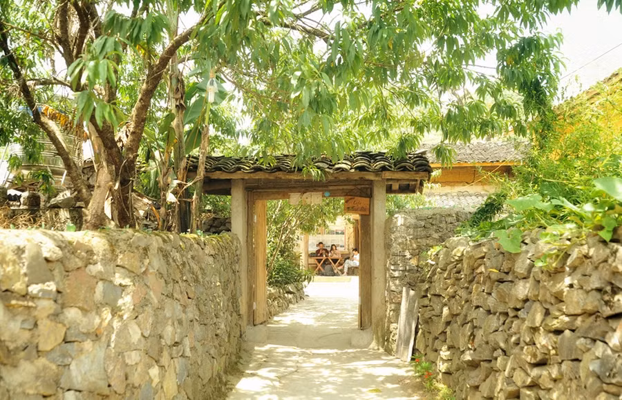 Cổng dẫn vào ngôi nhà, quán cà phê của chị Vấn. Bao quanh bởi tường rào đá, quán mang không gian kiến trúc theo phong cách truyền thống của người Lô Lô, nhà trình tường đắp đất, mái phủ ngói âm dương.