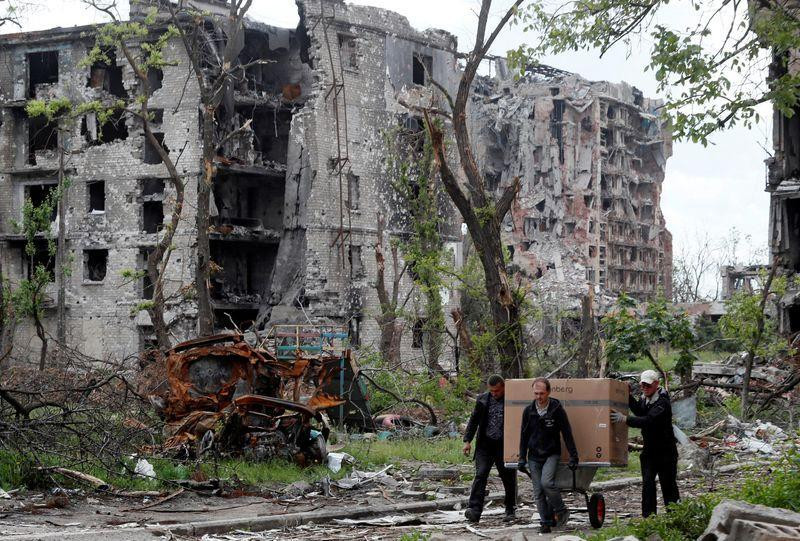 Cư dân địa phương vận chuyển một chiếc hộp trên xe kéo qua một tòa nhà chung cư bị hư hỏng nặng ở Mariupol. Ảnh Reuters