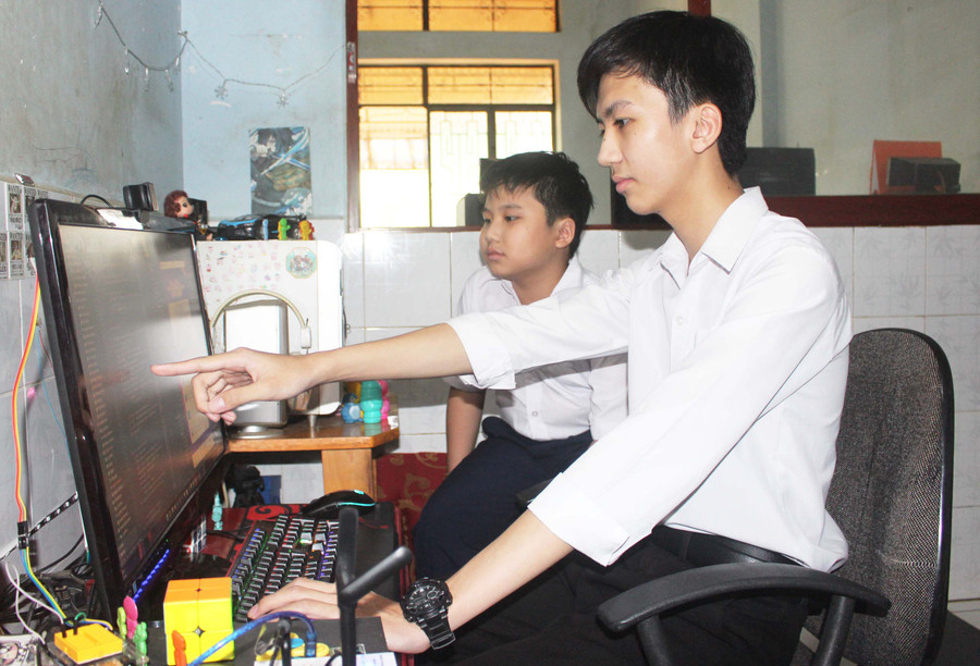 Em Trần Đăng Khoa (bìa phải) chia sẻ với em trai về lập trình “Ứng dụng học ngôn ngữ và hỗ trợ giao tiếp cho người câm/điếc”. Ảnh: Phan Lài