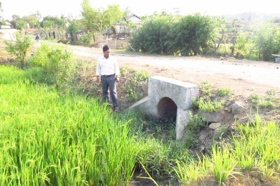 Ông Kruôi bên cạnh con đường dẫn vào cánh đồng của làng được ông vận động nhân dân đóng góp tiền, công sức làm cống, đổ đất. Ảnh: Hồng Thương Ông Kruôi bên cạnh con đường dẫn vào cánh đồng của làng được ông vận động nhân dân đóng góp tiền, công sức làm cống, đổ đất. Ảnh: Hồng Thương