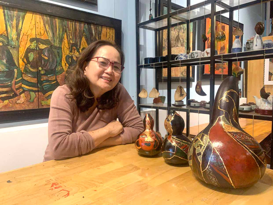 Hoạ sĩ Hồ Thị Xuân Thu bên những tác phẩm sơn mài trên quả bầu khô. Ảnh: Phương Duyên