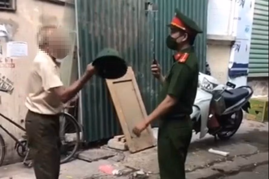 Hình ảnh ông cụ dùng mũ cối đánh vào mặt trung uý công an khi bị nhắc nhở đeo khẩu trang. Ảnh cắt từ clip Hình ảnh ông cụ dùng mũ cối đánh vào mặt trung uý công an khi bị nhắc nhở đeo khẩu trang. Ảnh cắt từ clip