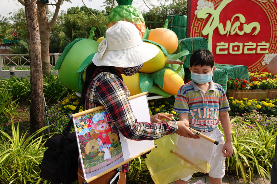  Một thợ chụp ảnh dạo giao ảnh lưu niệm cho khách nhí ở đường hoa Cần Thơ. Ảnh: Duy Tân