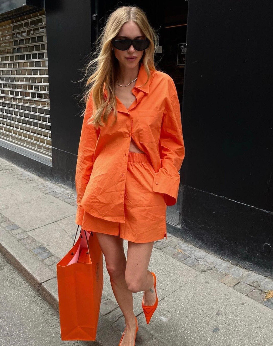 Mix chiếc áo sơ mi màu cam cùng quần shorts cạp cao và giày cao gót mũi nhọn sẽ cho bạn vẻ ngoài rực rỡ. Kính râm đen, dây chuyền vàng đơn giản và chiếc túi hàng hiệu Hermès càng tô điểm cho diện mạo thời thượng.