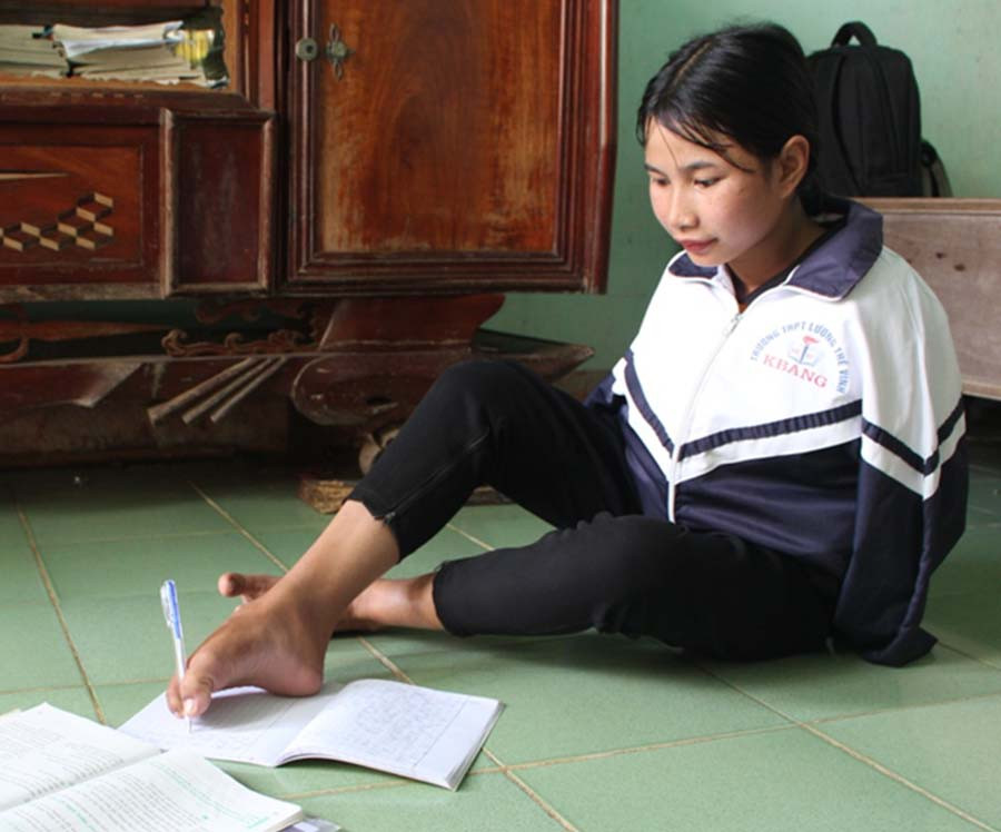 Không được may mắn như những người khác, Hlonh phải viết chữ bằng chân. Ảnh: P.L