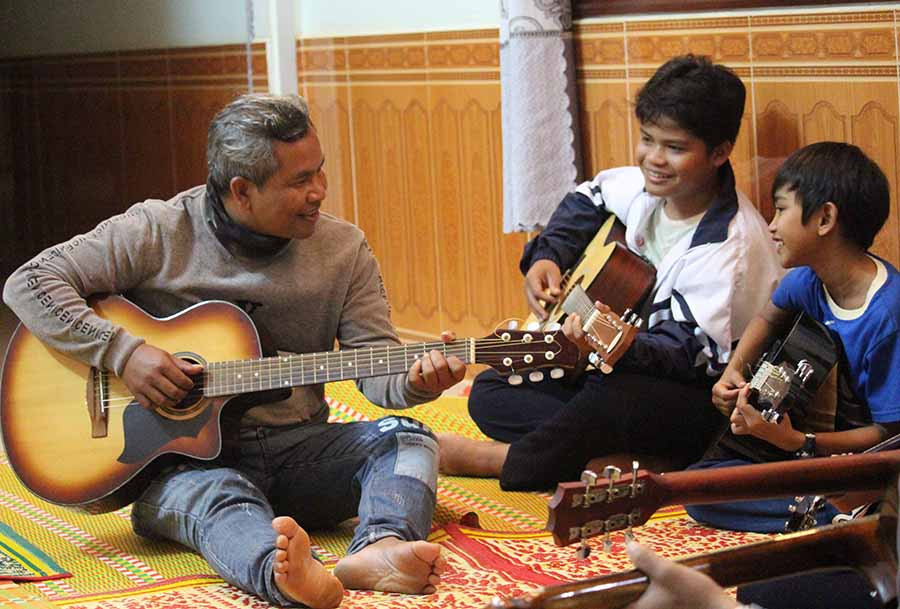  Anh Y Ploi (bìa trái) dạy đàn cho các em học sinh. Ảnh: H.S