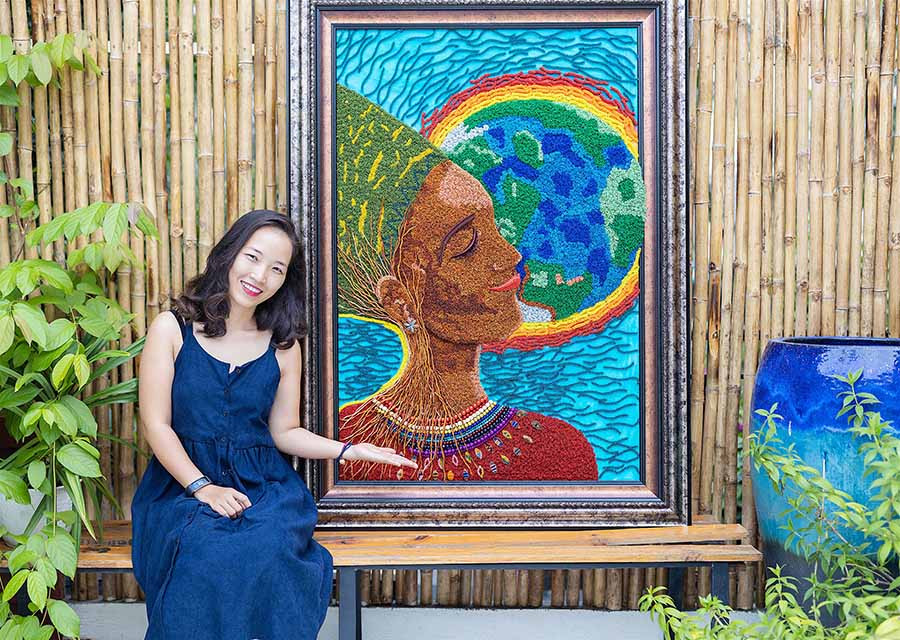 Phương Uma bên bức tranh "Mẹ trái đất" được quấn bằng dây đồng do chị tạo nên. Ảnh: M.T ” được quấn bằng dây đồng do chị tạo nên. Ảnh: M.T