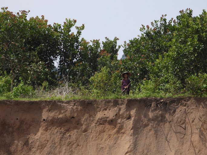 Một người dân cầm gậy đứng canh trên bờ để xua đuổi các tàu hút cát