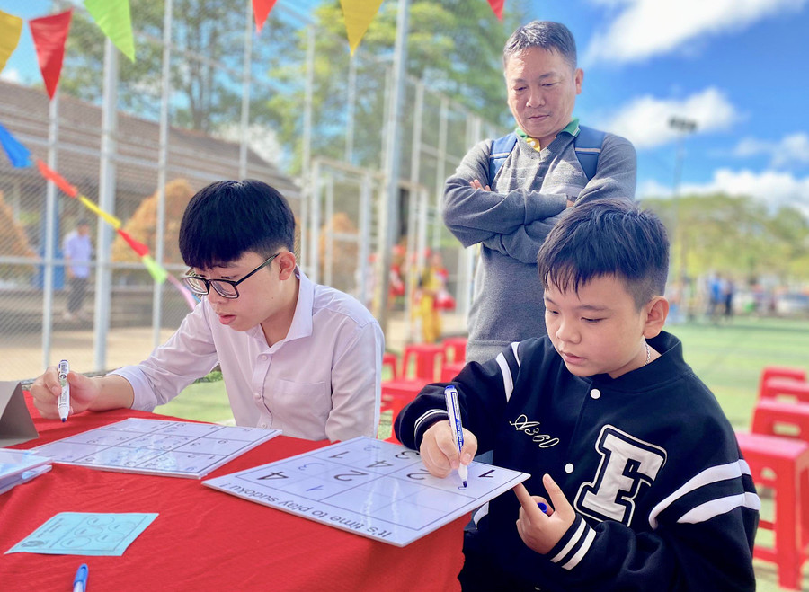 Ông Phan Anh Dũng (tổ 3, phường Diên Hồng, TP. Pleiku) chăm chú dõi theo con trai (áo đen) đang thử sức với trò Sudoku. Ảnh: Mộc Trà