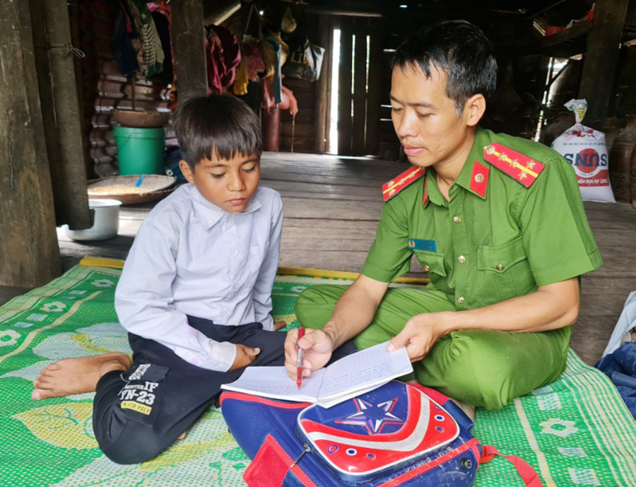 Cán bộ Công an xã Pờ Tó hướng dẫn em Đinh Phiên học bài. Ảnh: R'Ô HOK  Cán bộ Công an xã Pờ Tó hướng dẫn em Đinh Phiên học bài. Ảnh: R'Ô HOK