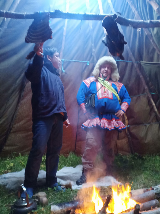 Tác giả cùng anh Niilas Sara và món thịt tuần lộc hun khói trong lavvu dưới chân đồi ẢNH: KHANG NGUYỄN